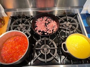 Pots of polenta with tomato/beans cooking, and a pan of pancetta in the background