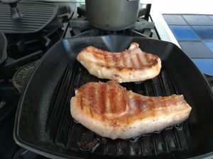two pork chops cooking on a grill pan