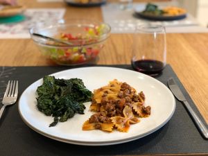 pasta with meat sauce next to kale, served with wine