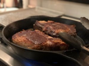 two large steaks cooking in a cast iron skillet